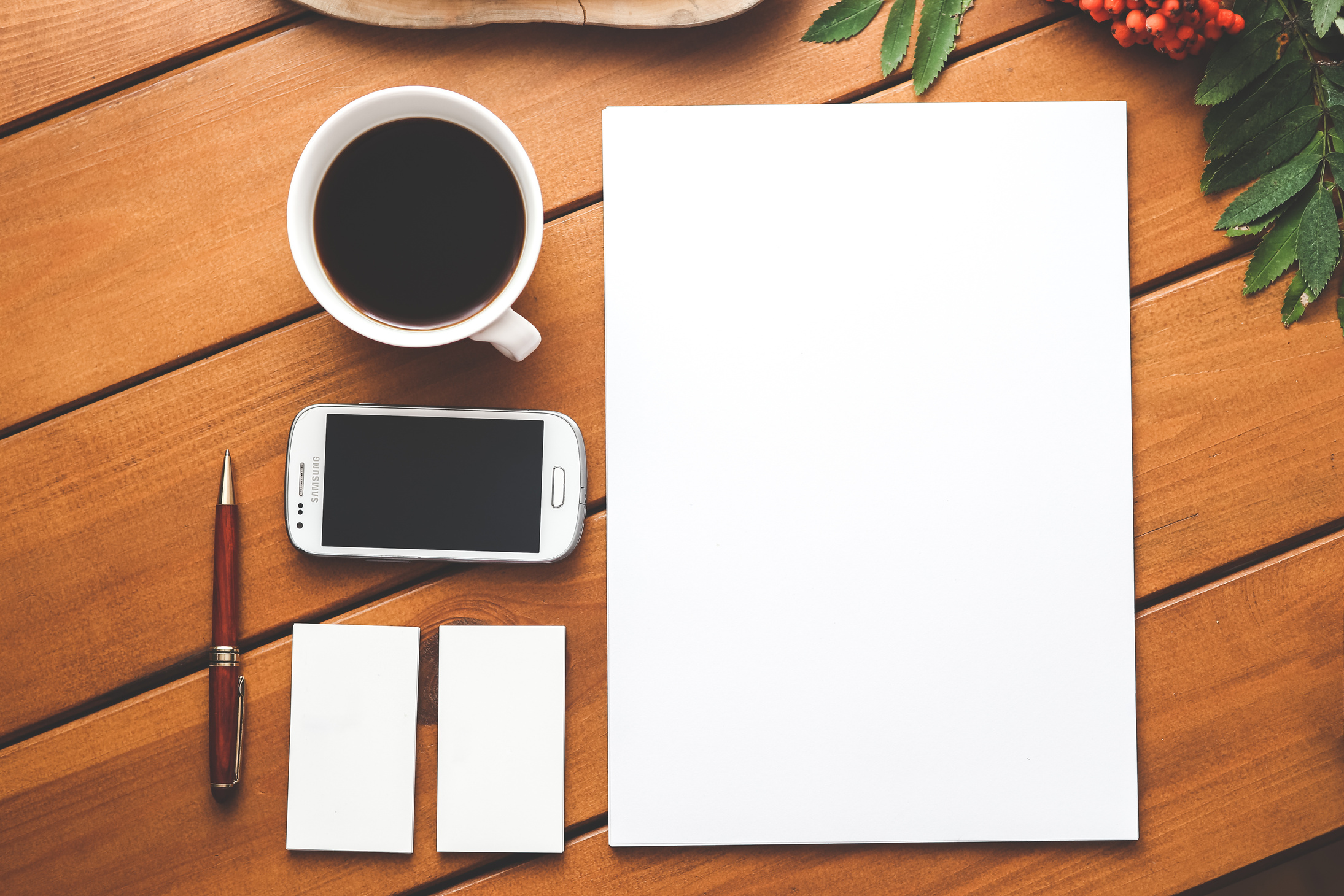 Smartphone surrounded with paper pen and cup of americano